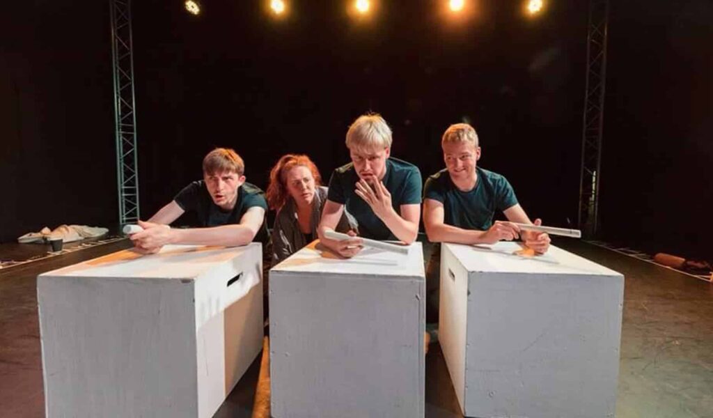 Four people leaning over boxes on stage looking at each other