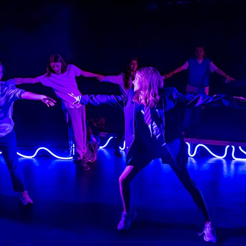 Youth Theatre performing on stage holding hands with blue lights