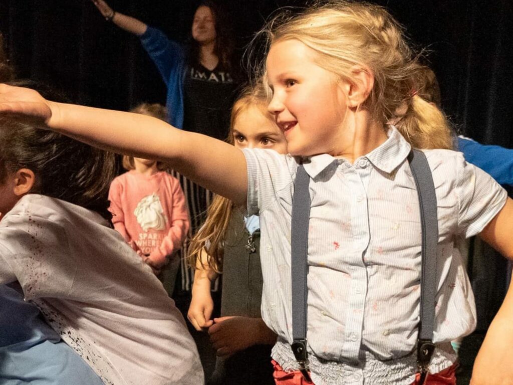Young actor on stage presenting hand in front of them with other children behind